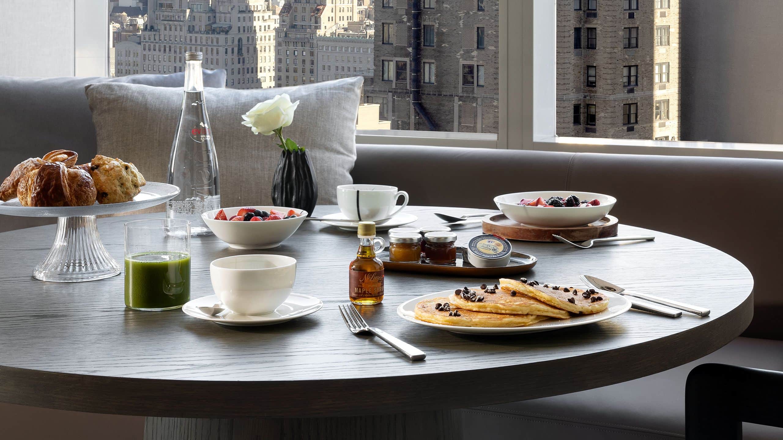 1 of 1 In suite dining nook with bench, chairs, and a table with breakfast food overlooking New York city