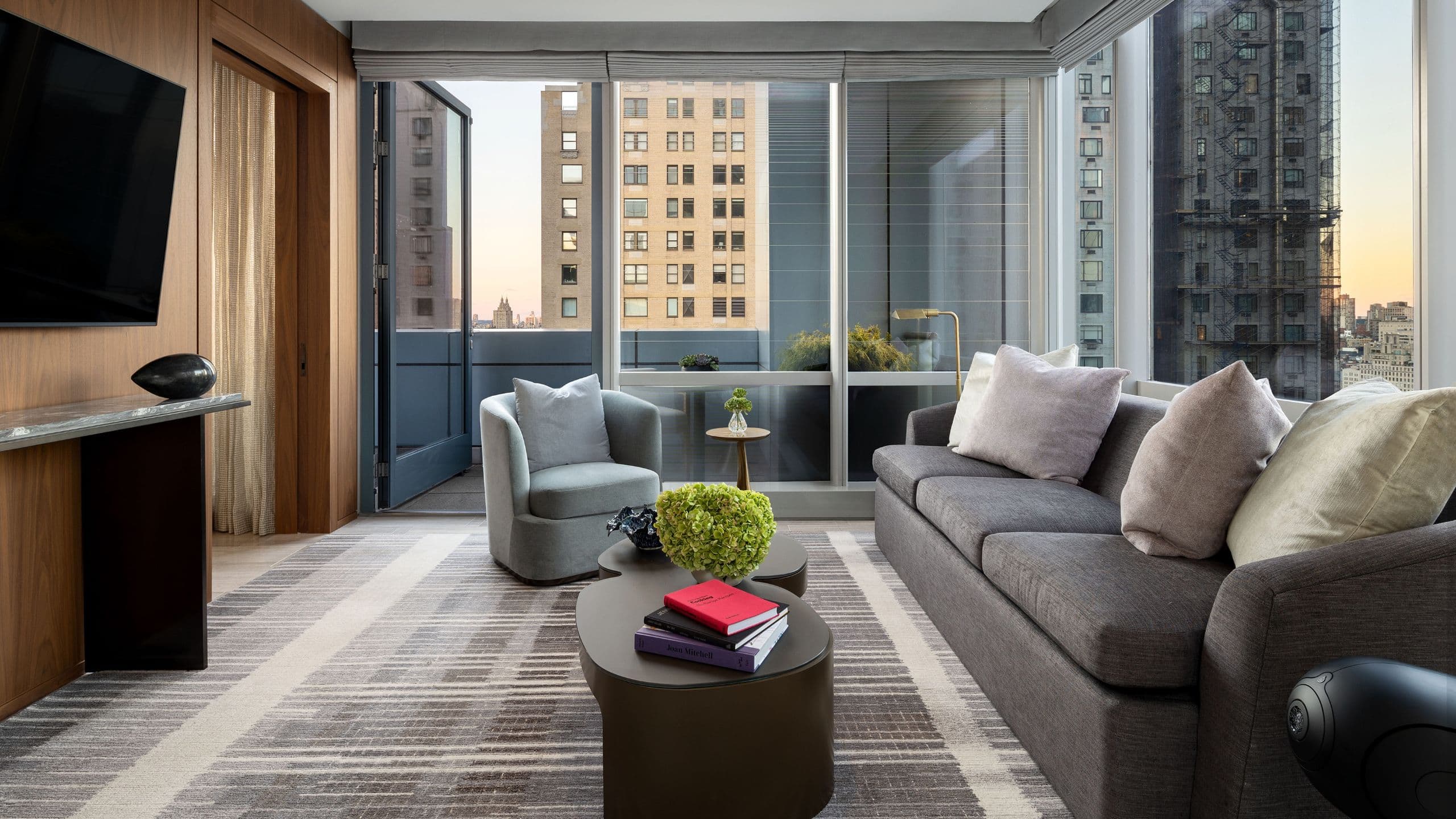 Elegant suite with dark gray sofa, coffee table, TV, and balcony overlooking Central Park