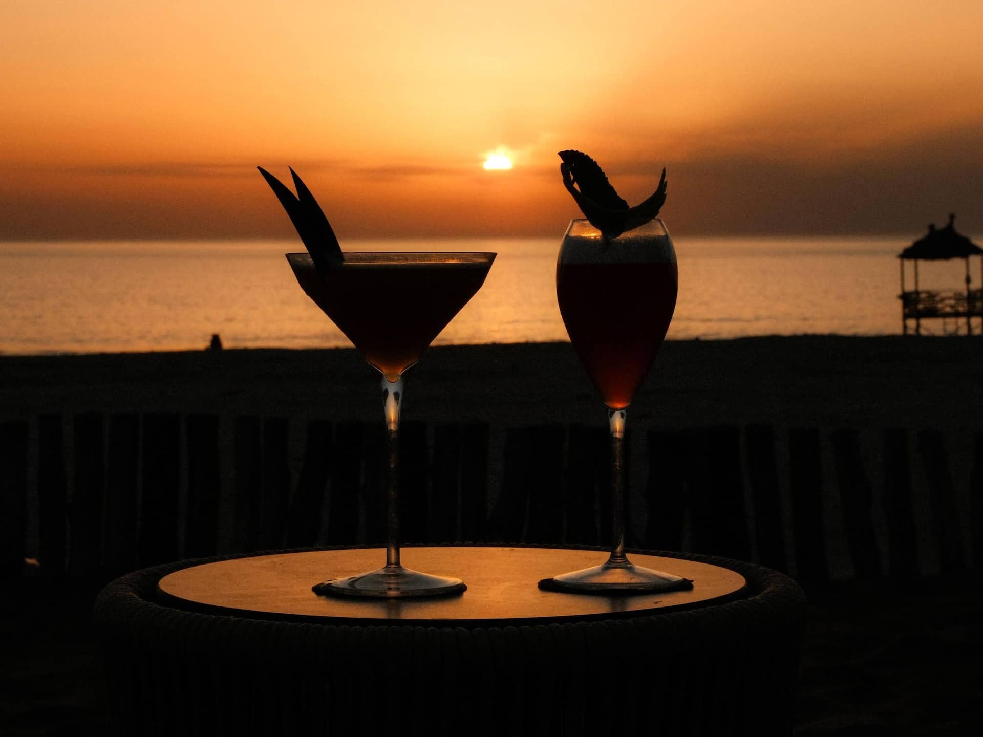 Two cocktails by the sunset, with vibrant colors reflecting in the sky