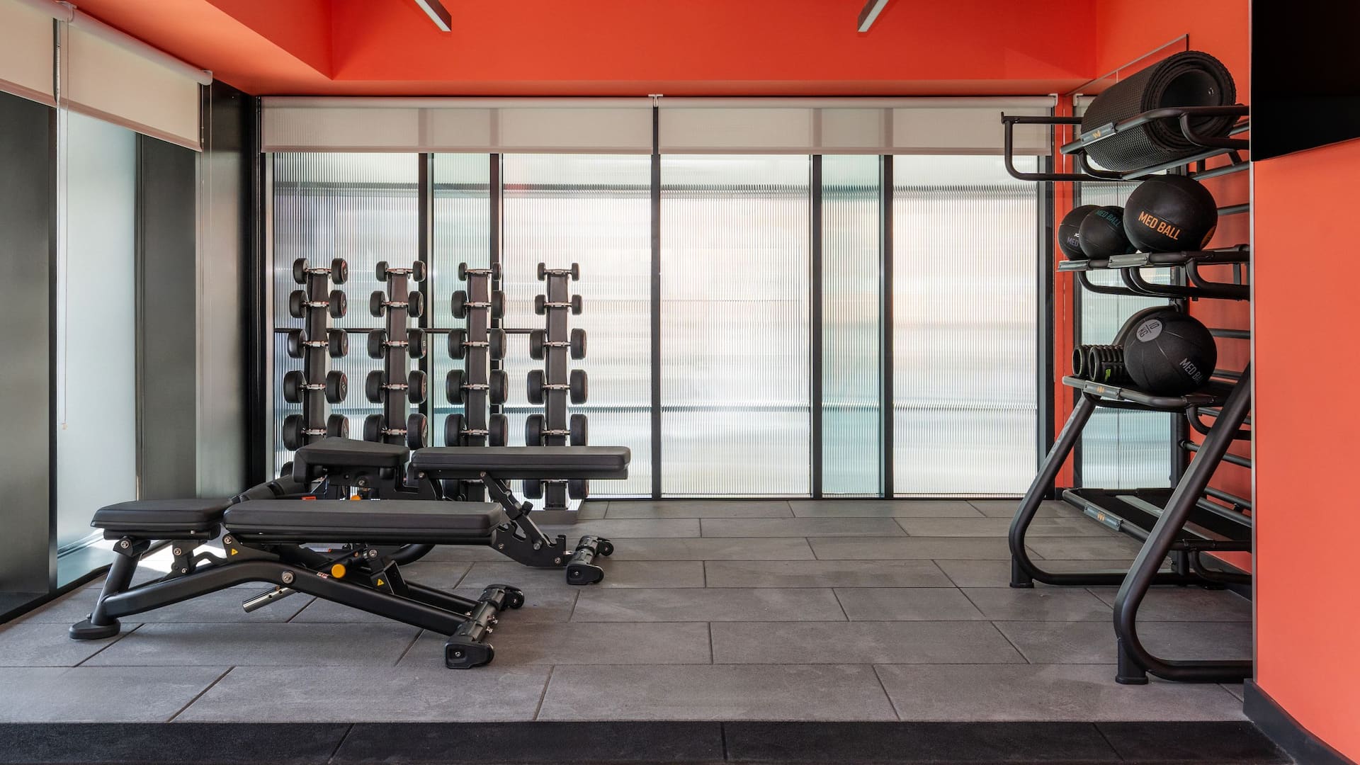 Well-equipped fitness centre with benches, dumbbell racks, and a bright orange ceiling.