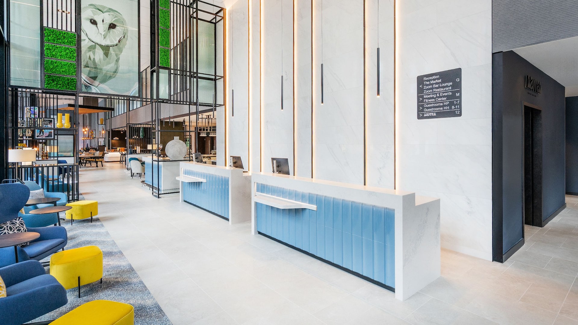 Modern hotel reception area at Hyatt Place Leeds with light blue desks, white marble walls and a lounge area of blue and yellow cushioned chairs.
