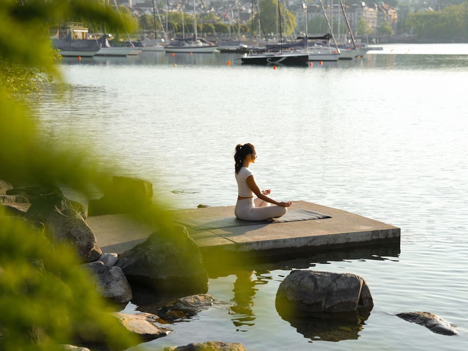Meditating woman by Lake Zurich in a sunrise setting