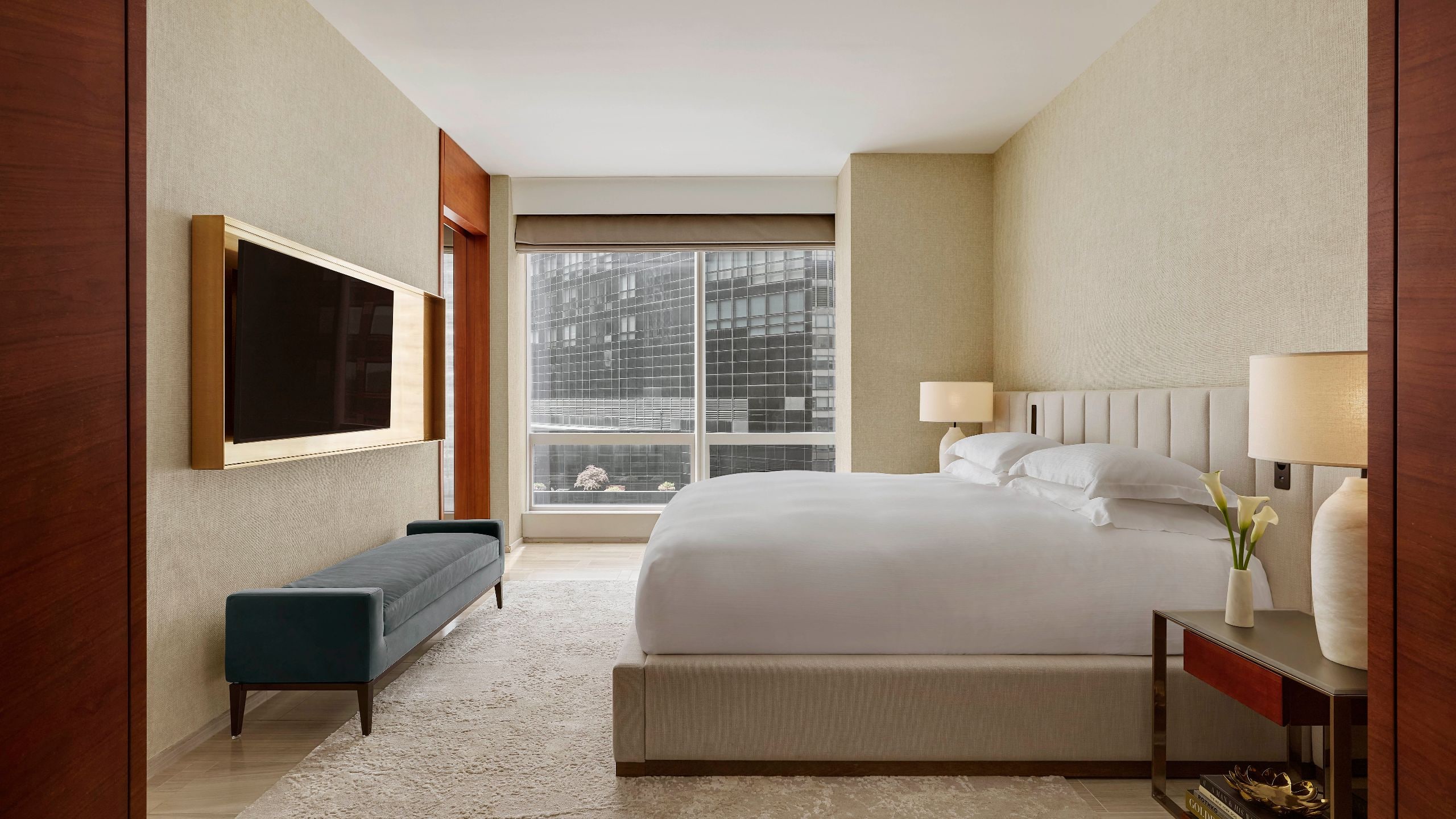 4 of 6 Streamlined bedroom with a king bed, velvet bench, neutral palette, and floor to ceiling city view
