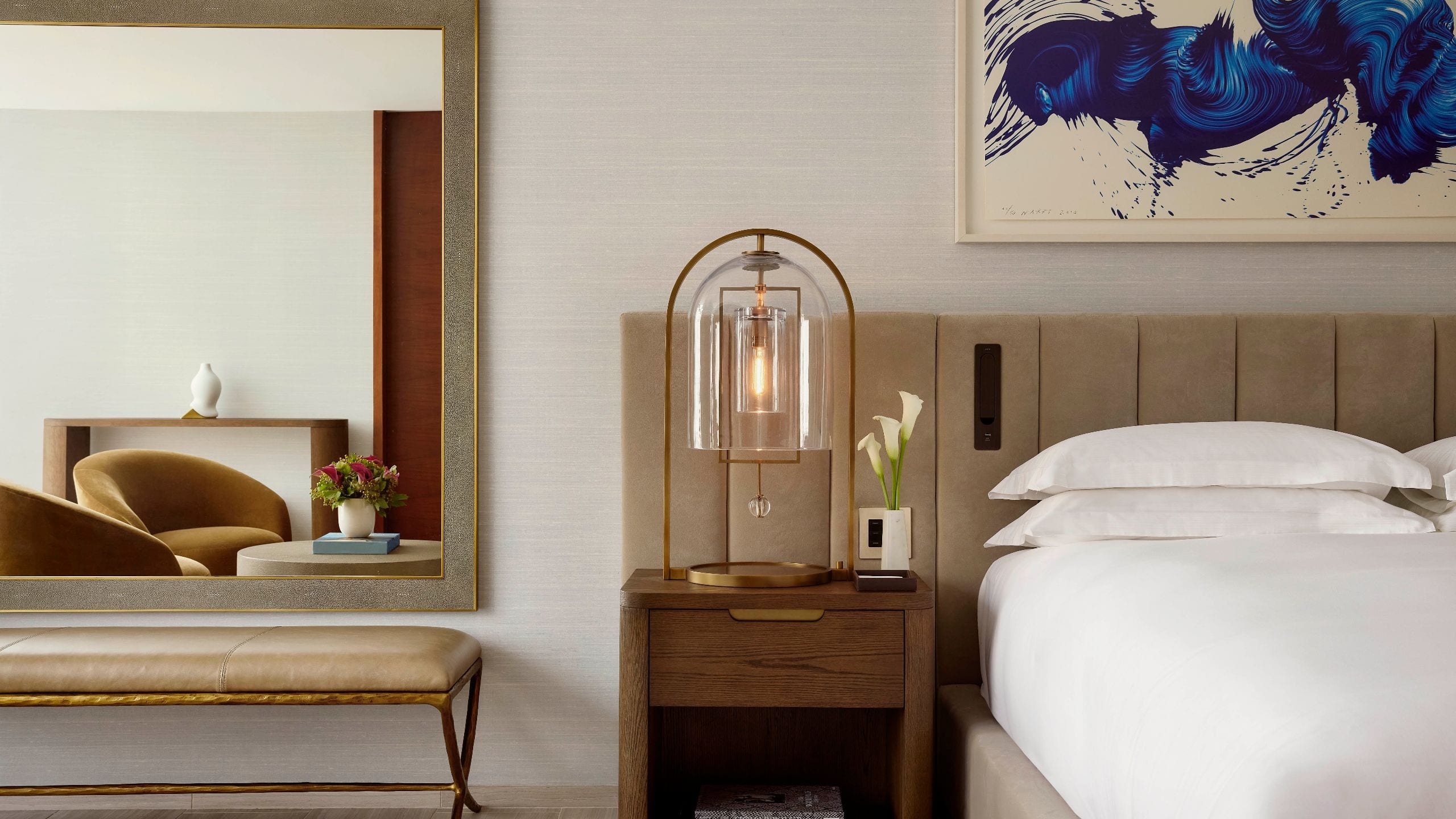 3 of 7 Close up of nightstand with modern lamp, calla lilies, and design books next to a velvet headboard