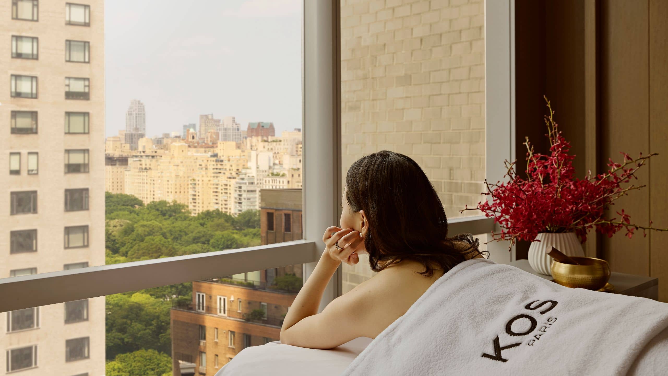 KOS spa products arranged on a wood tray beside fresh florals in a light filled suite with park views