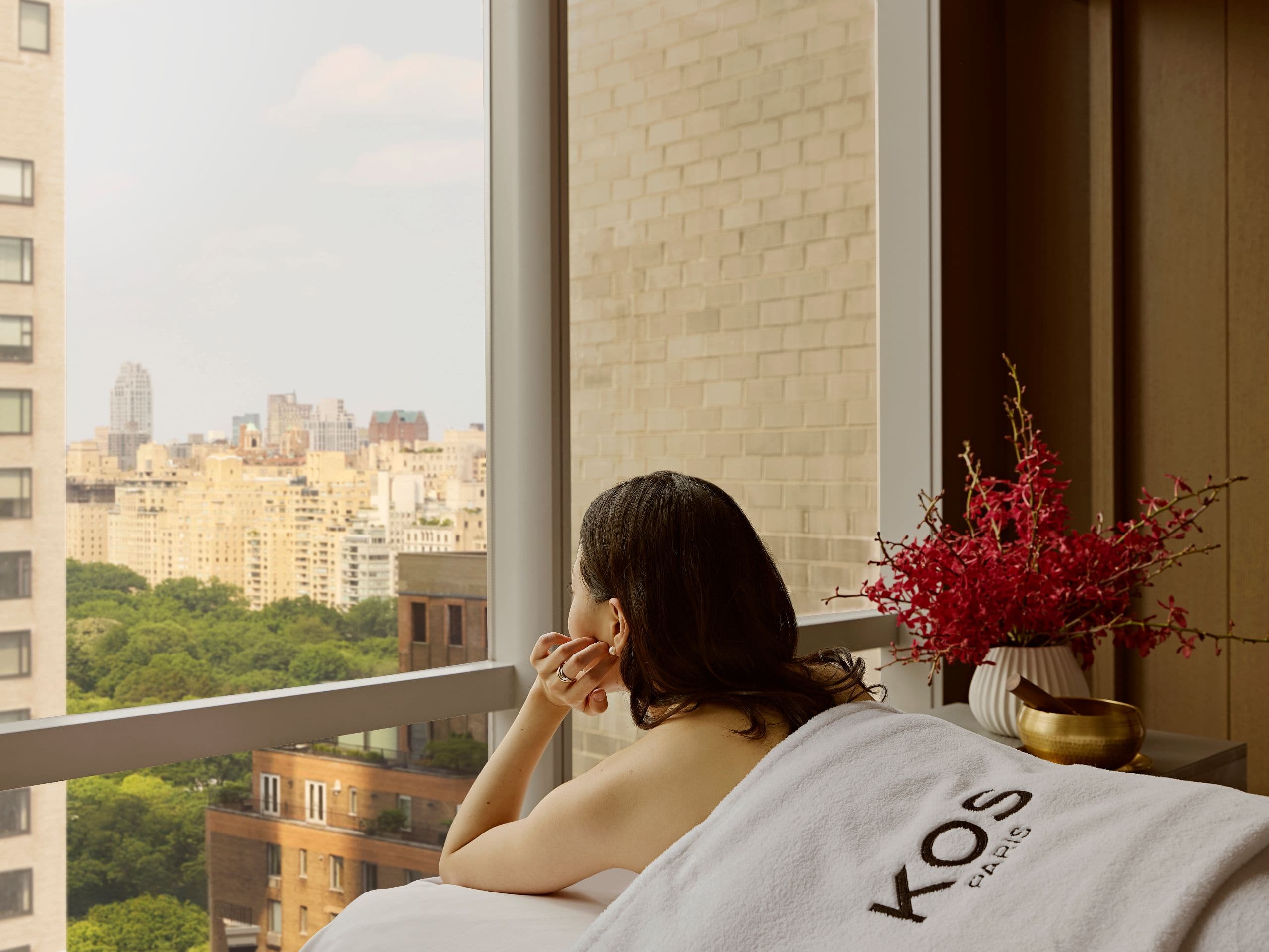 KOS spa products arranged on a wood tray beside fresh florals in a light filled suite with park views